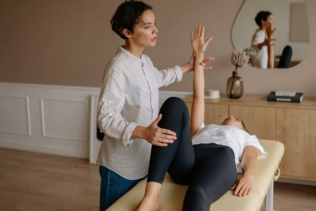 A physiotherapist guiding a patient through a shoulder movement on a treatment table in a bright consulting room.